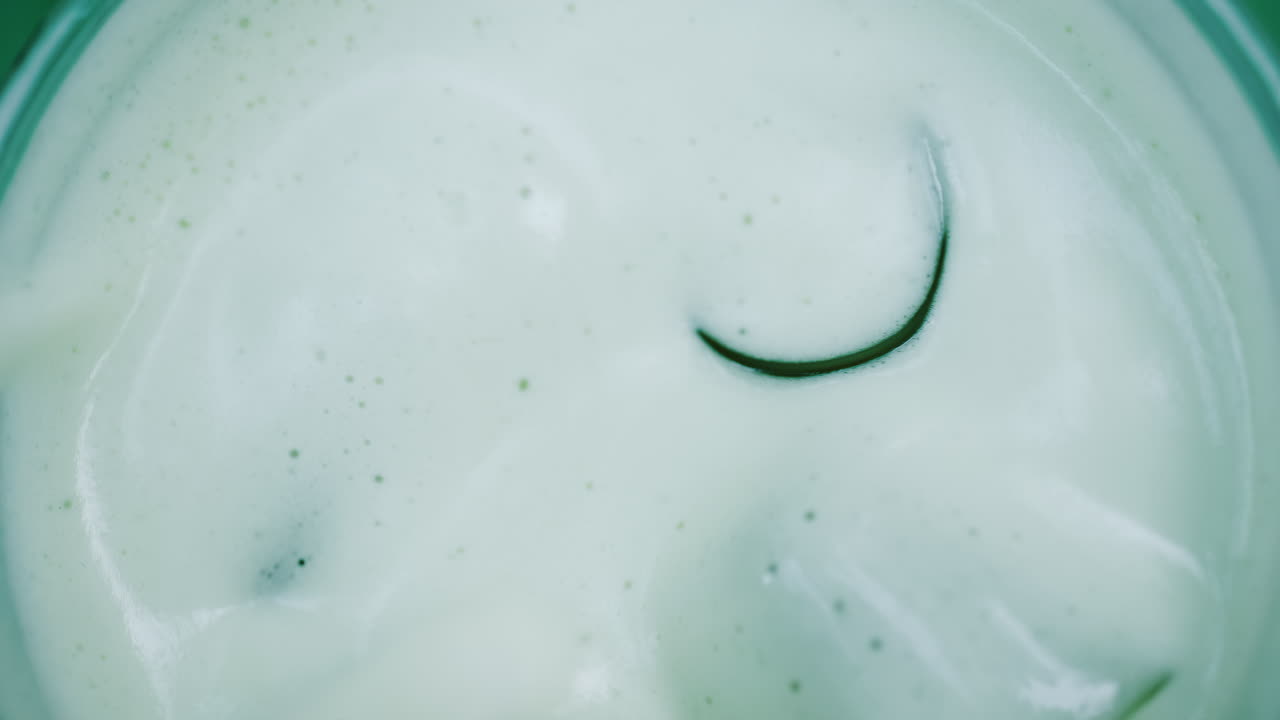 Close up of a white liquid being stirred in a glass with ice
