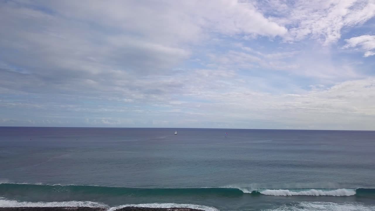 Veduta aerea di una barca a vela solitaria in un vasto oceano con cieli azzurri e nuvole.