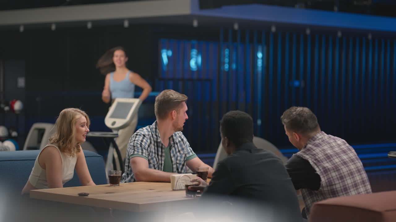 una mujer alegre corre a los amigos dando cinco grupos étnicos diferentes de personas sentadas en una mesa en un club de bolos. para celebrar y felicitar por la victoria y la racha anotada. danza de la victoria