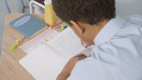 over the shoulder shot of an boy sitting at desk and writing in notebook during english class at school