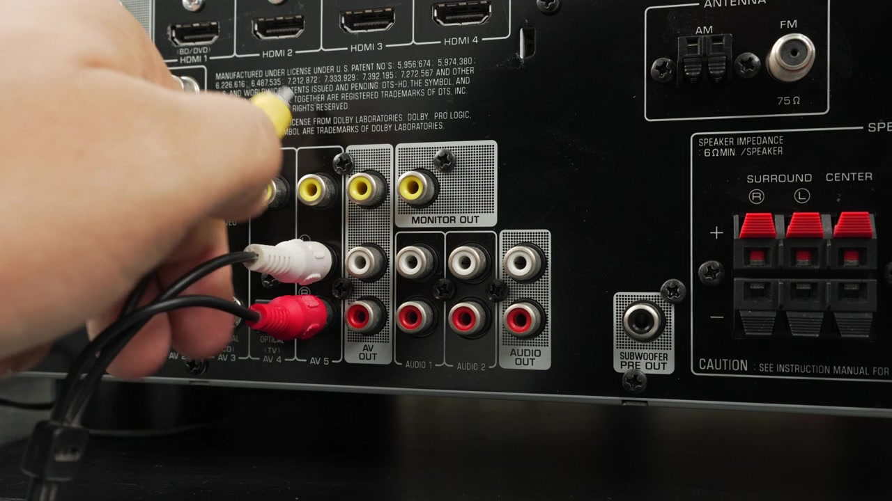 Mano maschile collega cavi RCA gialli e rossi nelle porte di uscita monitor di un ricevitore video, enfatizzando le connessioni analogiche e la configurazione dell'home entertainment
