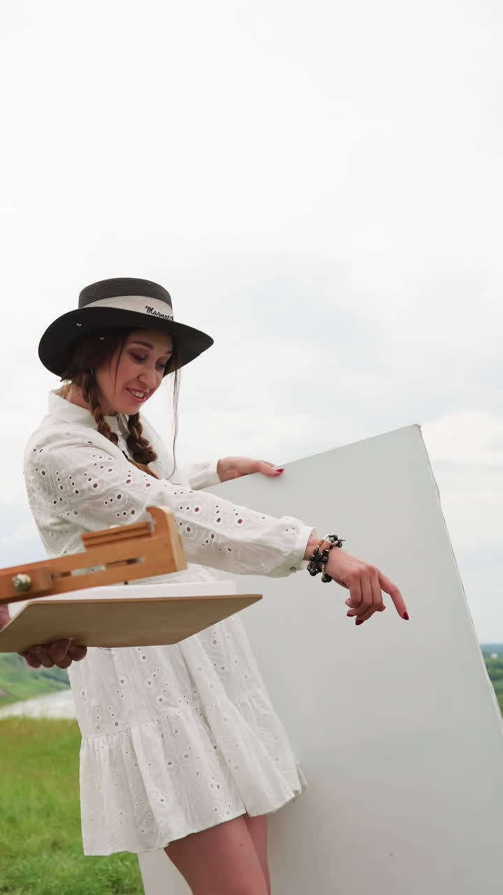 캐주얼 아티스트 의상을 입은 남녀가 그림을 그리는 장비와 함께 잔디을 고 있습니다. 남자는 체크 셔츠, 청바지, 검은 페도라를 입고, 스을 들고 있습니다. 여자는 에 미소 짓고 있습니다.