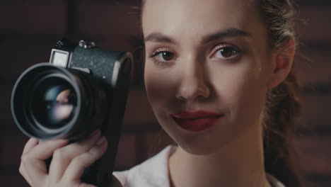 Stylish-woman-photographer-with-retro-photo-camera-smiling-into-camera-in-studio