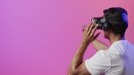 Video-of-biracial-man-using-vr-headset-on-pink-and-purple-background