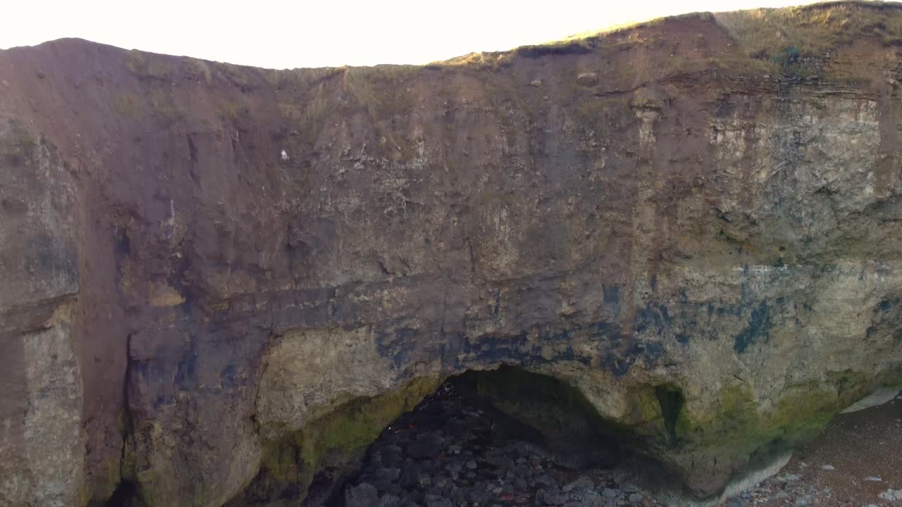 Zoom out shot of a coastal cove, eventually rising above the cliff tops in South Shields.
