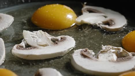 macro shot of sliced champignon mushrooms on eggs in a pan, sprinkled with salt, cayenne, and black pepper