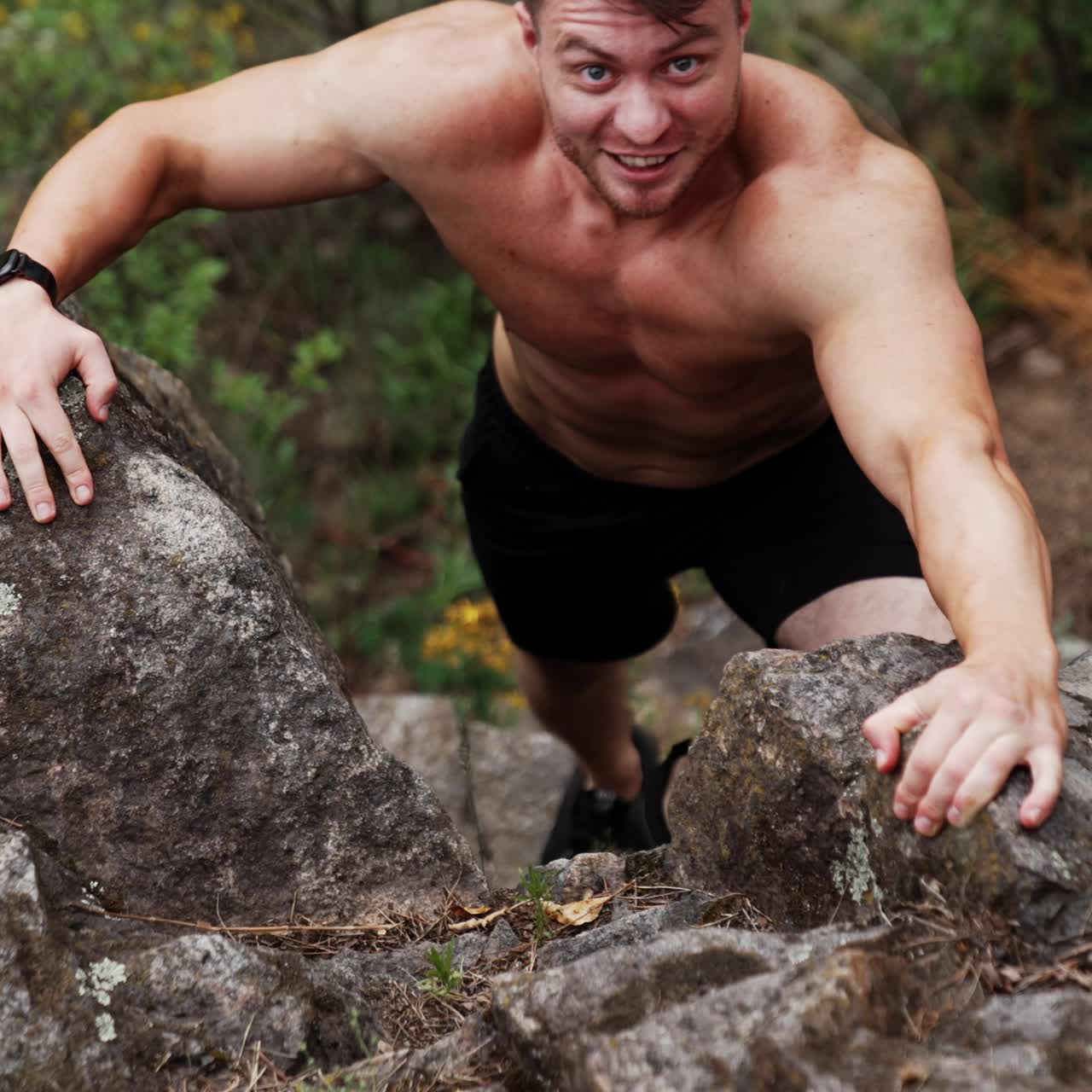 Sportive Caucasian man with naked torso climbs the high rock. Strongman uses nature surrounding for work out