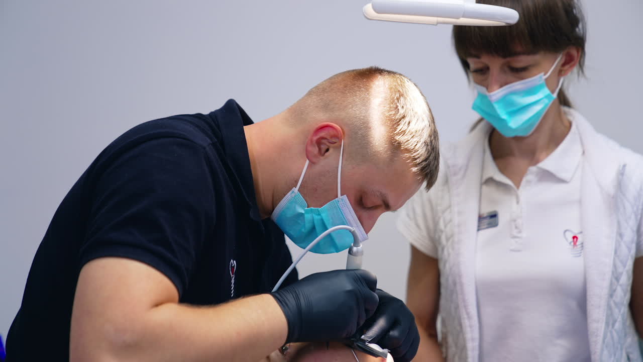 Stomatologist doing dental procedure to a patient. Male dentist and assistant in masks treating teeth in medical centre. Healthy teeth.