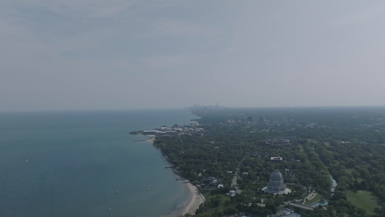 Wide aerial footage of the coast of Lake Michigan with the Baháʼí House of Worship in the foreground and Chicago in the hazy background
