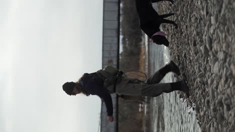 Vertical-format:-Man-with-dog-fly-fishes-in-river-near-rail-bridge