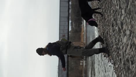 vertical format: man with dog fly fishes in river near rail bridge