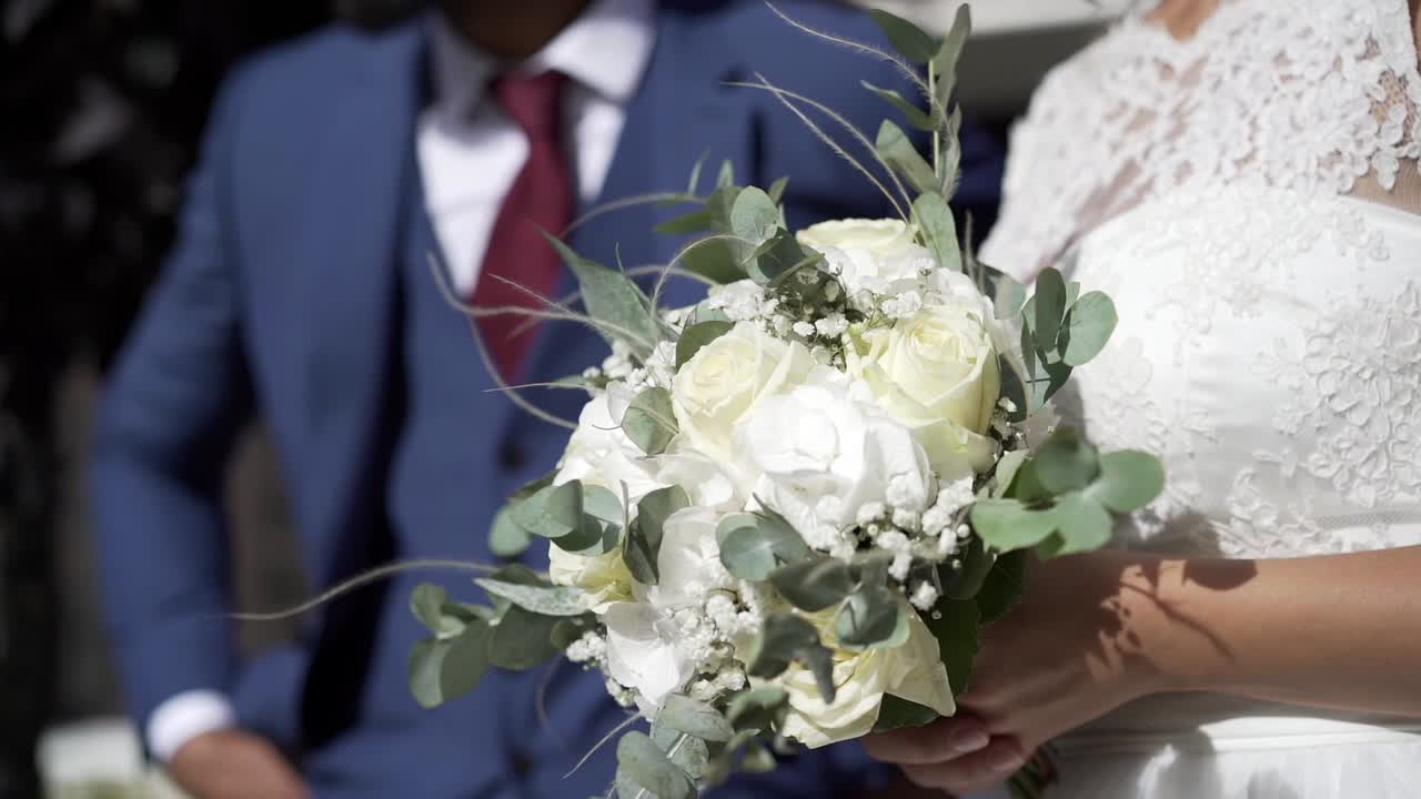 Sposa con un bellissimo bouquet di fiori in mano e uno splendido abito bianco, uomo in abito blu in piedi accanto a lei e fuori fuoco