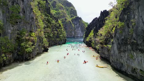 tourists kayak swim in ocean bay, calm water lined with black sea cliff