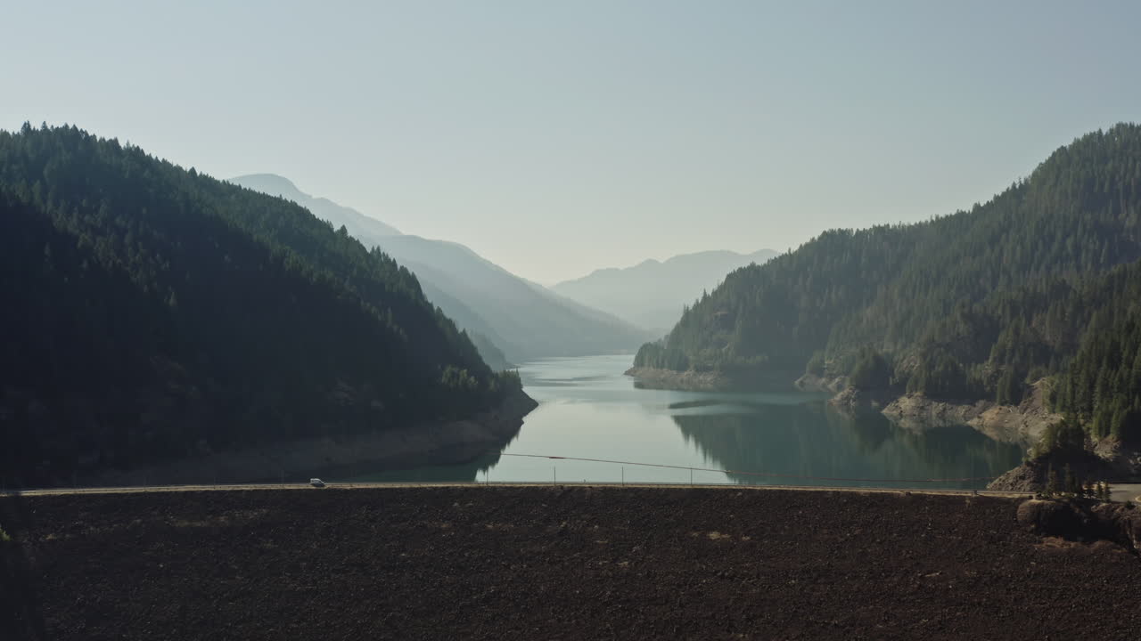 Camper van drives across dam leading to Cougar Reservoir in Oregon on hazy summer day.