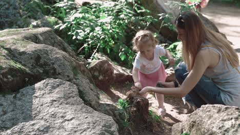 young beautiful mother with her daughter feeding a chipmunk in the woods among stones 2