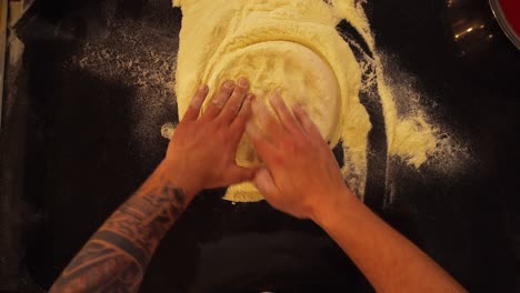 overhead view of professional cook rolling pizza dough into a flat pizza bread. top down view of chef making pizza from corn flour