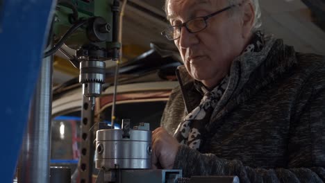 old worker preparing drilling machine in a small dark workshop