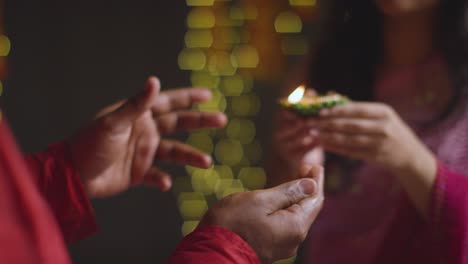 close up of woman handing lit diya oil lamp to man celebrating festival of diwali