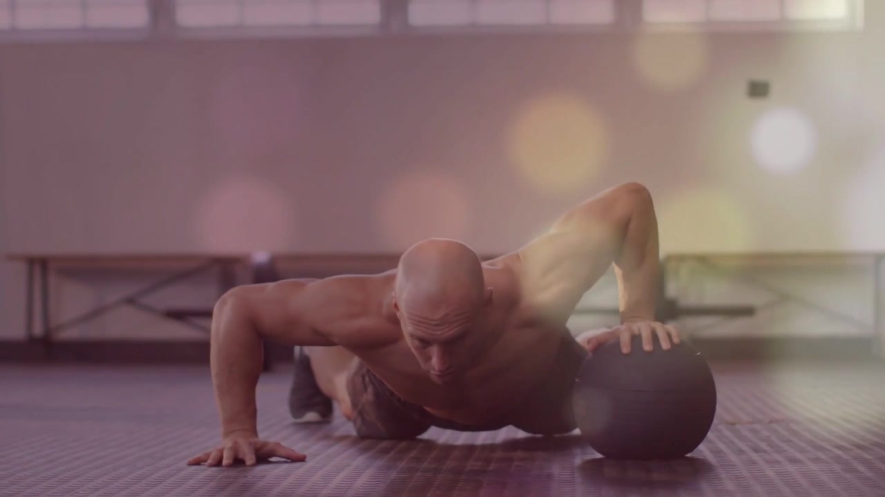 Uomo che inizia in posizione di appoggio su una palla medica facendo flessioni con un braccio solo per il fitness, che si ripete con una sovrapposizione bokeh.