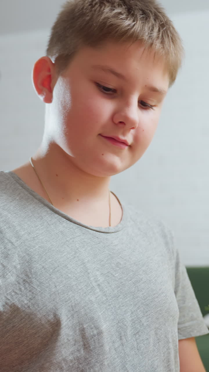 Кавказский мальчик использует планшет дома, мягкий дневной свет и серая рубашка создают спокойную домашнюю атмосферу, крупные планы показывают, как ученик делает домашнее задание, играет в казуальные игры, читает сообщения и делает наброски идей