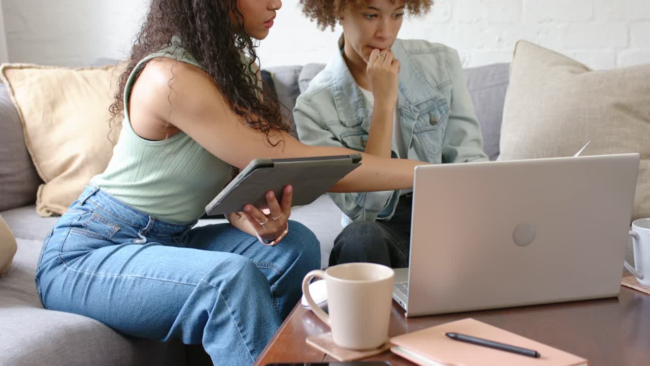Femmes afro-américaines assises sur un canapé, l'écran de la tablette au centre de l'attention, désignant un ordinateur portable, en train de prendre une décision