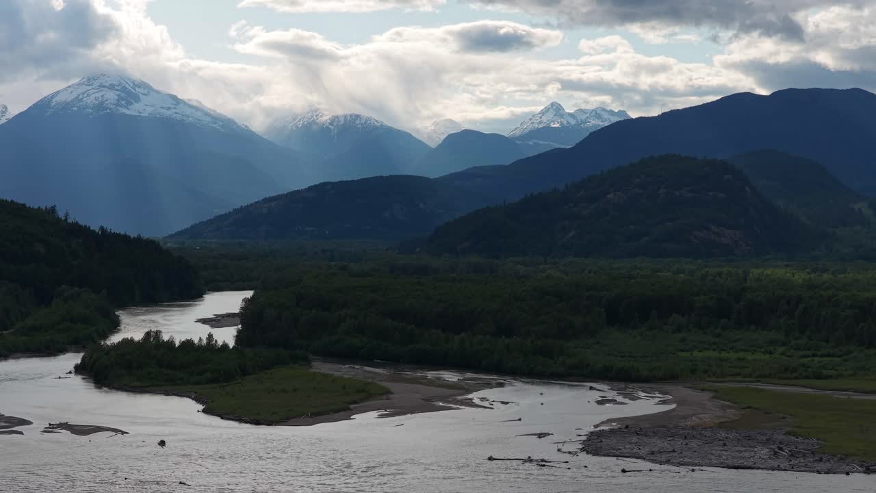 Scenic river flowing through a valley, surrounded by lush green forests and snow-capped mountains in BC, Canada.
