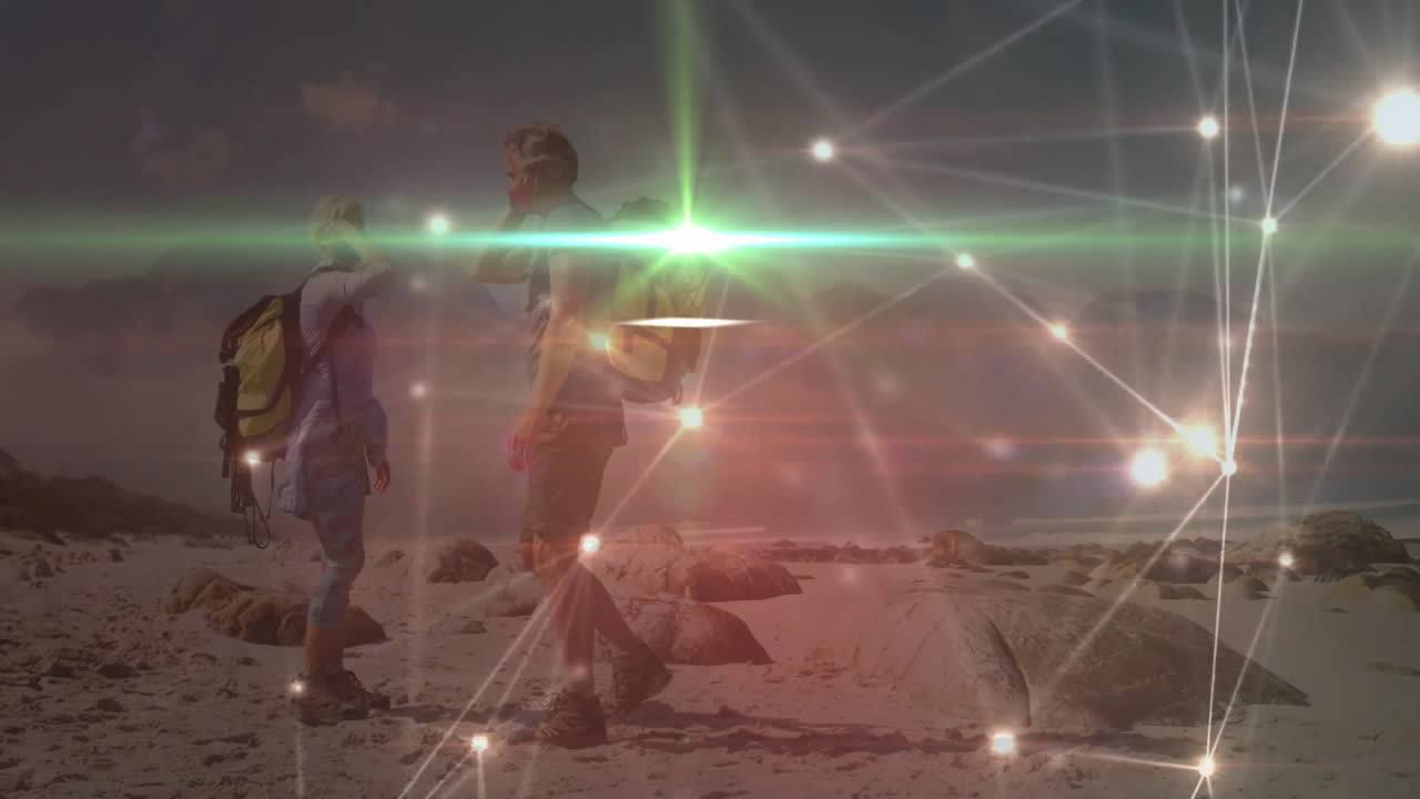 Couple hiking on rocky coastline while glowing tech data points linking backpacks under dusky sky