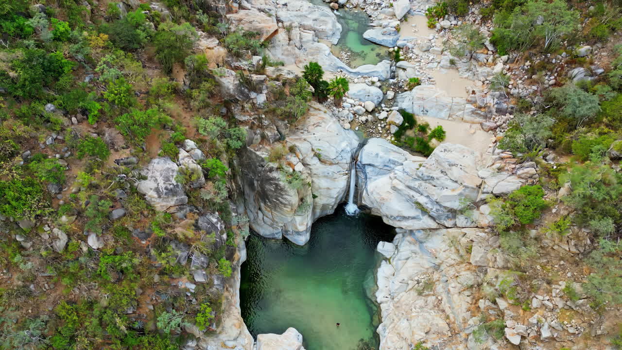 Aerial drone view of a canyon with a small waterfall falling into a natural pool surrounded by rocky cliffs in Baja California, Mexico