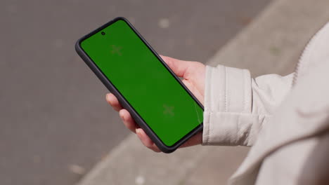 sobre el hombro disparo de cerca de la mujer al aire libre en la calle de la ciudad sosteniendo un teléfono móvil de pantalla verde