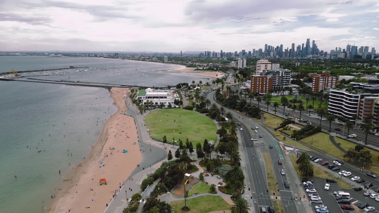 Drone footage capturing an approach along St Kilda Beach, with vehicular traffic and an approach towards the Melbourne City.