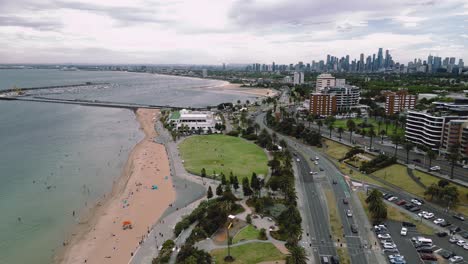 drone footage capturing an approach along st kilda beach, with vehicular traffic and an approach towards the melbourne city.
