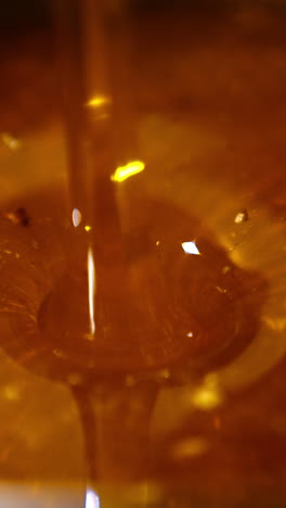amber honey flowing into the dish. beautiful fresh organic product being poured onto the metal sieve for cleansing. vertical video
