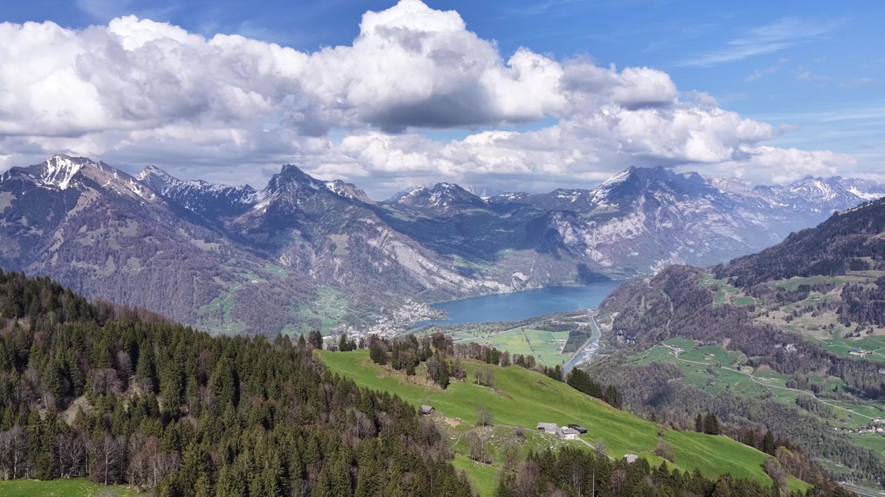 Ampio panorama aereo con vista su un lago alpino blu, foreste ondulate e imponenti cime montuose nelle Alpi svizzere. Splendido paesaggio primaverile ideale per temi di viaggio e natura.