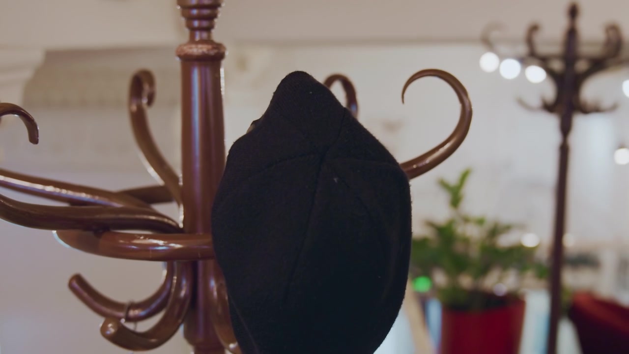 Primo piano di una persona che appende e sistema un cappello nero su un appendiabiti marrone decorato con illuminazione interna soffusa. La mano interagisce brevemente con il tessuto assicurando il corretto posizionamento tra gli altri ganci.