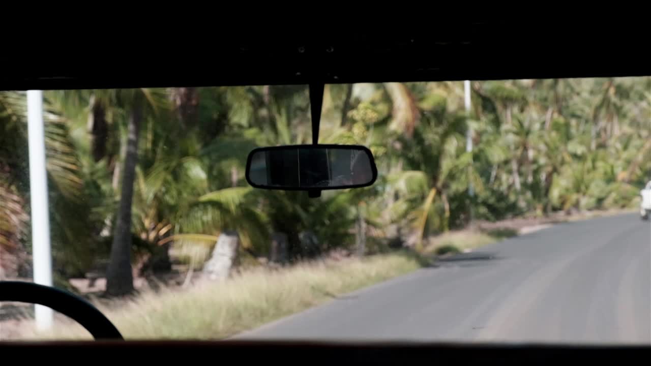 espejo retrovisor de un viejo landrover conduciendo por una carretera en una isla tropical con palmeras durante el día