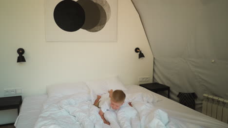 child jumps and fall on soft bed at glamping. playful little boy enjoys game in comfortable hotel bedroom. funny kid has fun in luxury camping tent