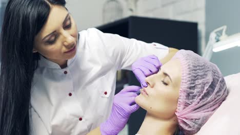 beautiful doctor in medical coat doing bottox injection to the lips of a young woman in beauty clinic. lips augmentation
