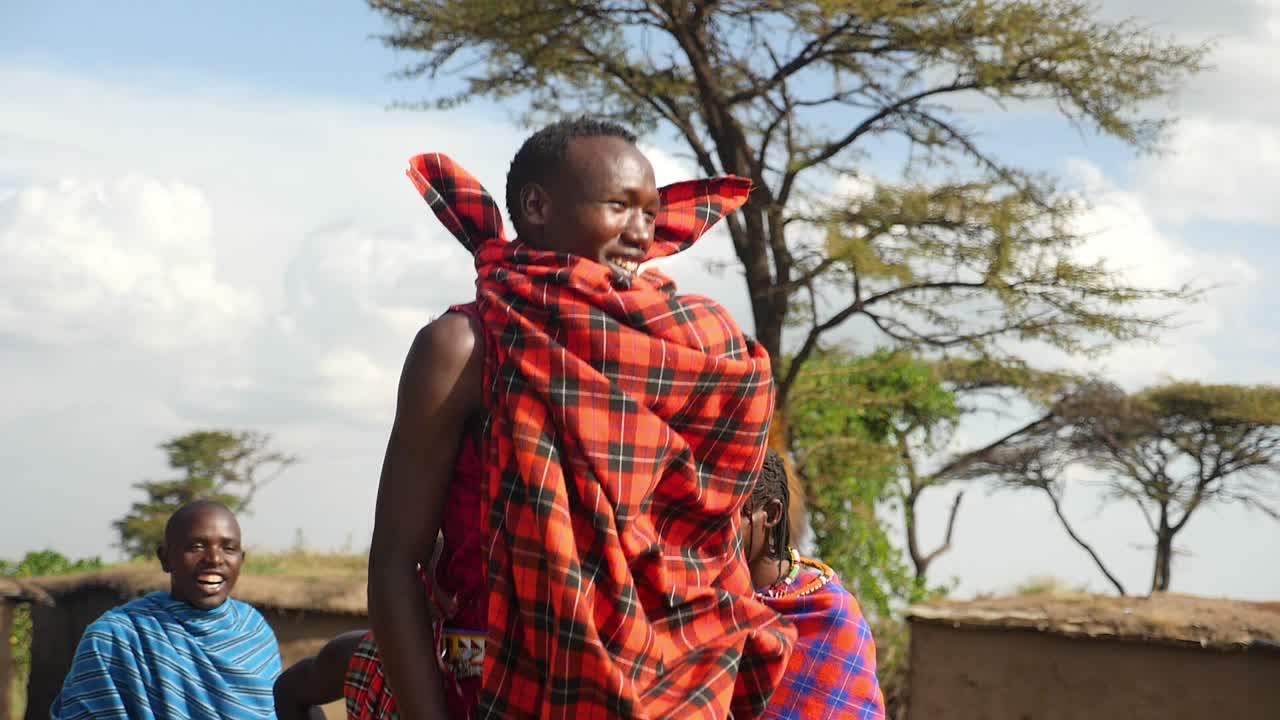 Maasai Tribal warriors perform their jumping dance in front of their village in Masai Mara , Kenya with tree in Background with Blue Sky
