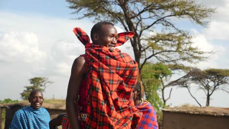 maasai tribal warriors perform their jumping dance in front of their village in masai mara , kenya with tree in background with blue sky