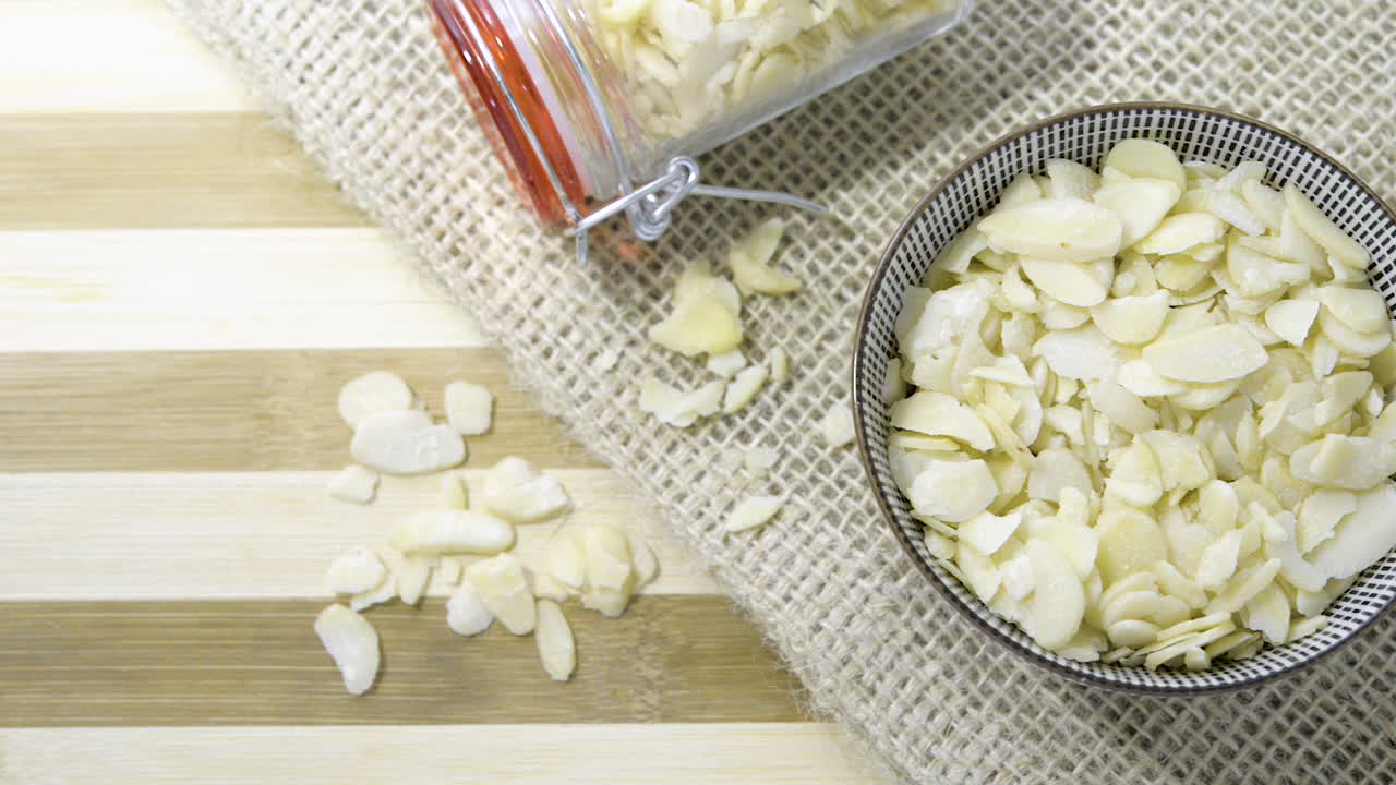 라미네이트 아몬드 너트로 채워진 유리병 세라믹 그릇이 있는 줄무늬 나무 테이블 헤시안 천을 가로지르는 느린 패닝 샷