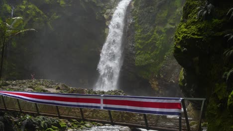 waterfall beside bridge with costa rica flag on top of mountain with river