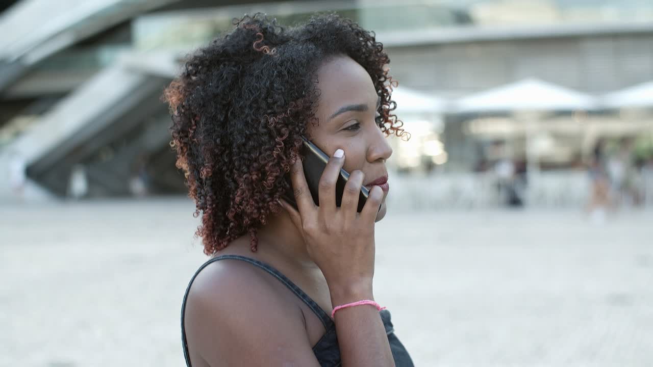 Mulher cacheada sorridente conversando com interlocutor pelo telefone