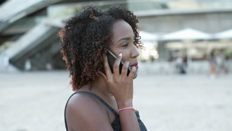 mulher rizada sorridente falando com o interlocutor através do telefone