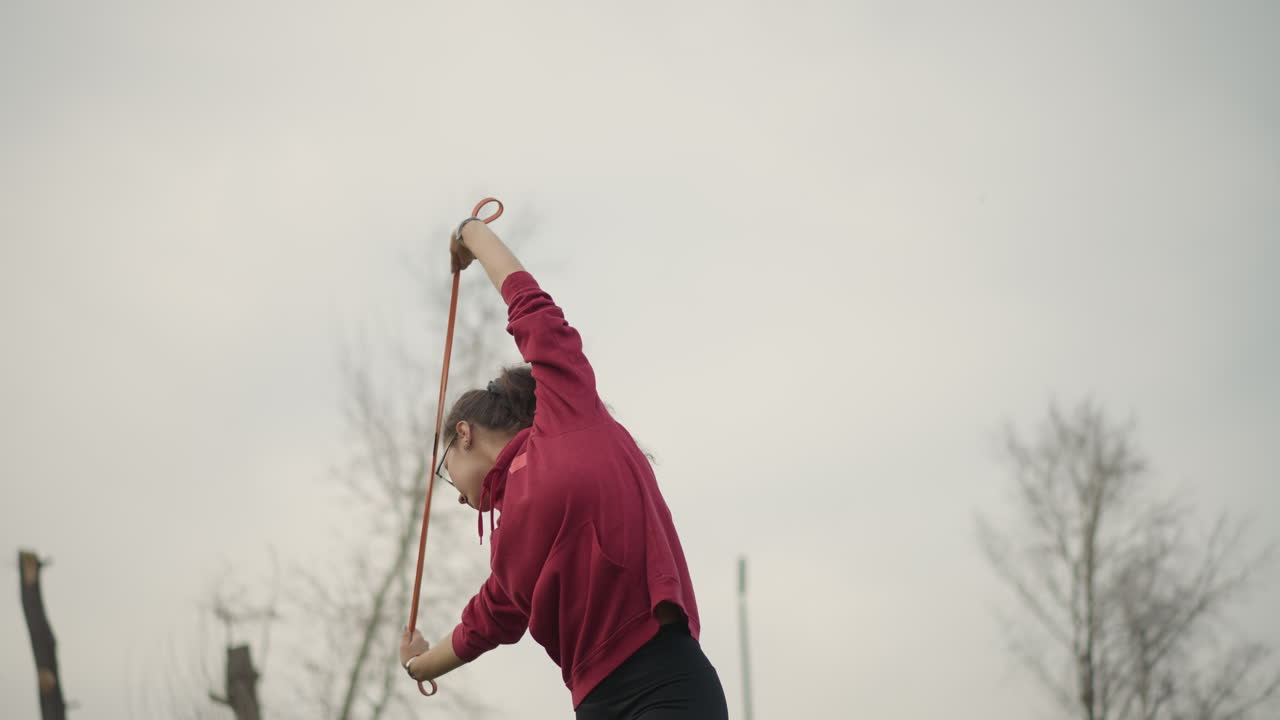 Silhouette Of Woman Flying Ribbon In Sky, Focused Lady Holding Ribbon Against Soft Cloudy Background Outdoors, An Outdoor Scene Capturing Woman Practicing With Ribbon Against Light Cloudy Sky