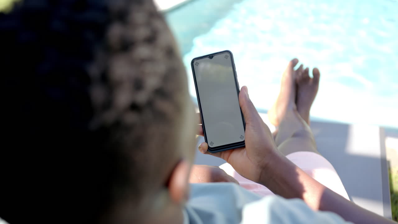 Relaxing by pool, person using smartphone while lounging on chair, copy space