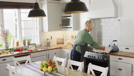 happy senior caucasian woman standing in kitchen and preparing dinner