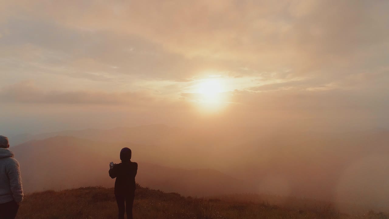el hombre y la mujer están de pie en la cima de la montaña contra el amanecer