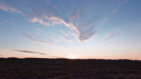 track forward, tilt up, sun setting behind the hills of mount isa in the outback with orange and blue sky and light clouds, mount isa, queensland, australia