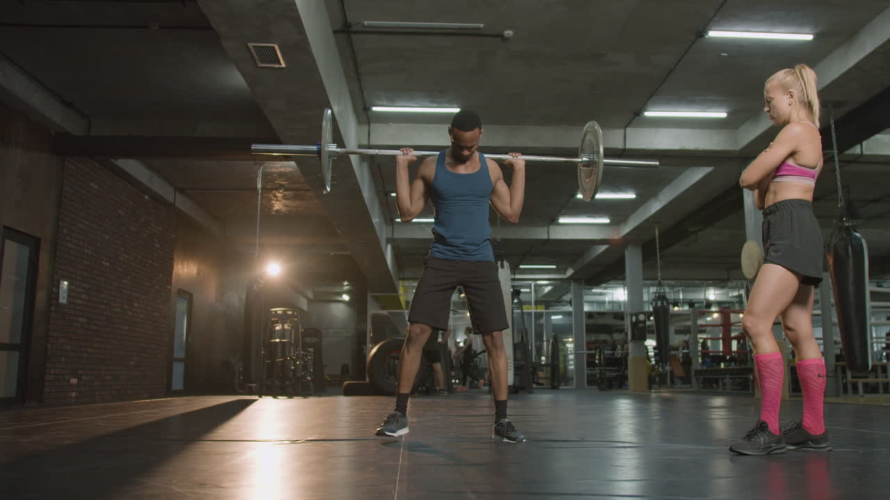 Distant view of caucasian female monitor and an athletic african american man in the gym.