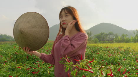 해가 지는 동안 농장 플랜테이션에서 일하는 동안 냉각하기 위해  모자를 사용하는 베트남 젊은 여성의 근접 초상화